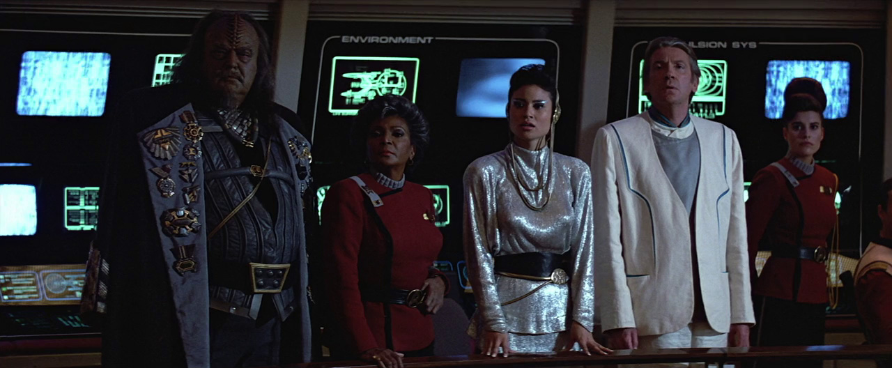Vyslanci Karrd, Dar a Talbot, v pozadí Uhura u komunikační stanice