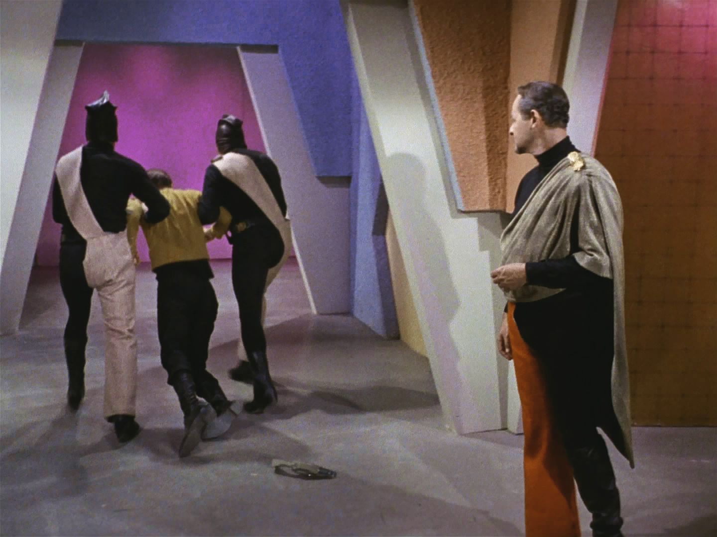 Výsadek si vedl dobře a Kirk chce získat komunikátory, spojit se se Scottym a varovat ho. Místo toho ho ale přemohly eminianské stráže a vyslanec Fox se bezelstně transportuje.