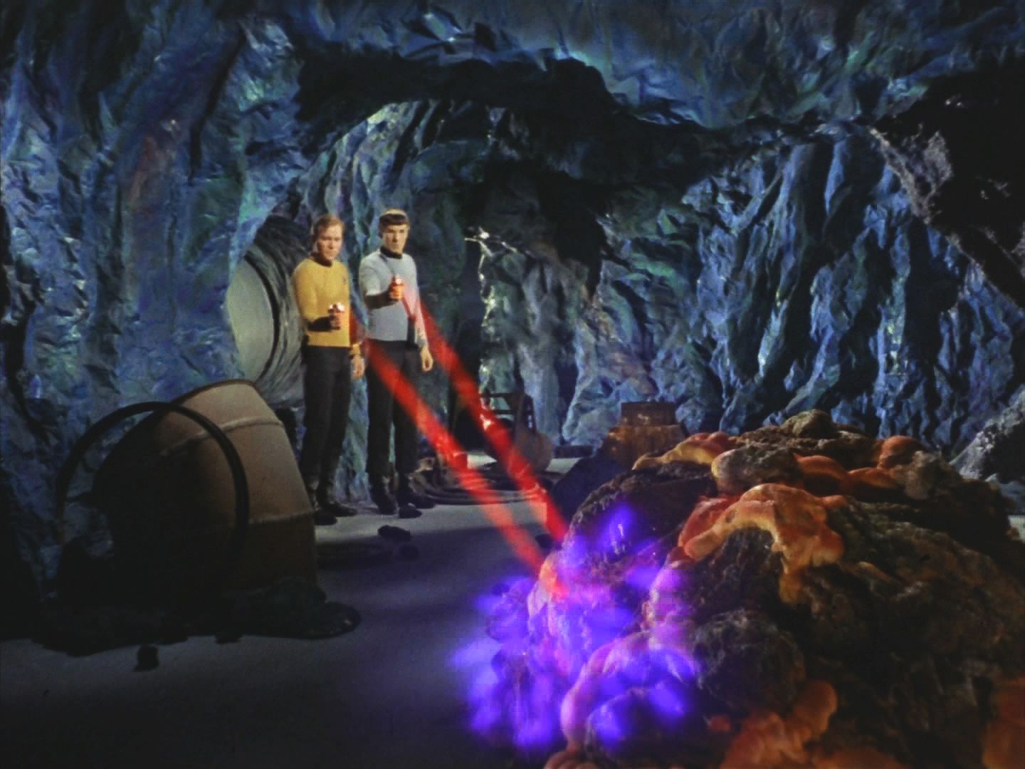 Posílený výsadek z Enterprise i horníci začínají pátrat po zabijákovi ve spletitém komplexu tunelů. Kirk a Spock na něj narazili a dvěma phasery ho zranili a přinutili k ústupu.