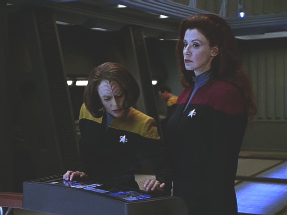 Q utrpěla zranění a není schopna vrátit se do Q kontinua vlastními silami. Jedinou možností je Voyager - posádka stejně musí přivést zpět unesenou kapitána Janewayovou.