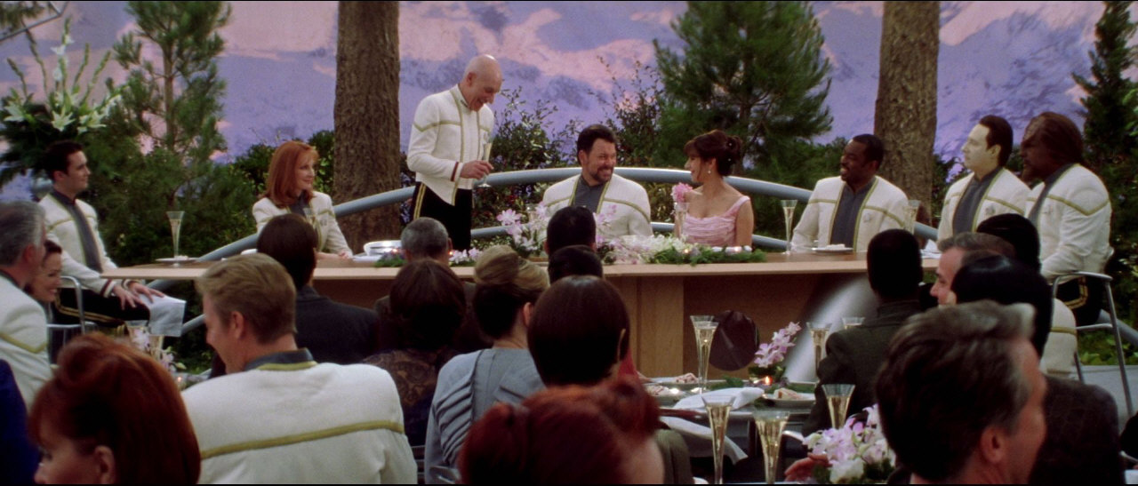 Kapitán Jean-Luc Picard předsedá večírku na počest svatby Williama Rikera a Deanny Troi.