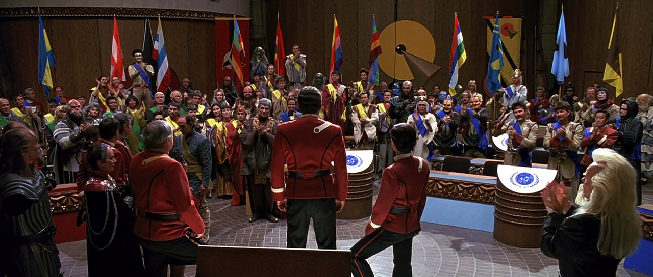 Posádka Enterprise v jednacím sále na Khitomeru, v pozadí romulanský velvyslanec Nanclus a vulkanský velvyslanec Sarek